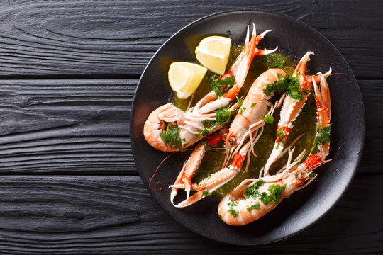 Gourmet seafood scampi or langoustine or Norway lobster are served on a black plate with sauce and lemon. horizontal top view