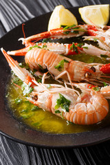 Cooked scampi or langoustine close-up on a plate with sauce and lemon on a table. vertical