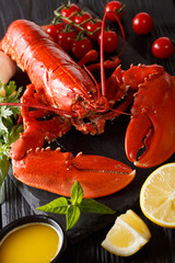 Delicious boiled lobster macro with lemon, fresh tomatoes and herbs on a black table. vertical