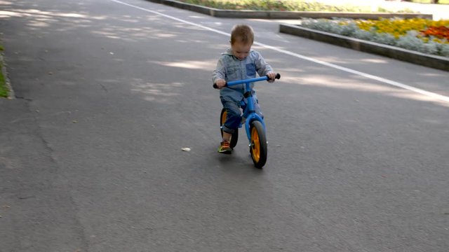 Slow motion 4k. A child rides a running bike in the Park. A little boy rides a balance bike in a city public Park.