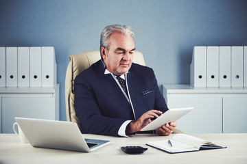 Mature entrepreneur working on tablet computer at his table