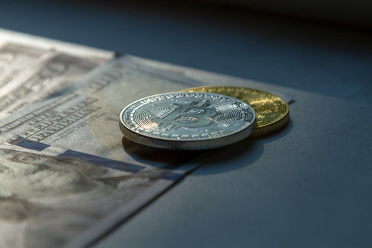 Coins bitkoin lie on dollar bills in the rays of the setting sun. The concept of bitcoin, crypto currency and dollars. Photo of dollars and coins bitcoin with beautiful light on a dark background.
