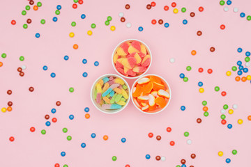 top view of paper cups with jelly candies and scattered dragee isolated on pink