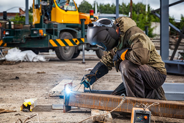 A young  man welder in brown uniform, welding mask and welders leathers, weld  metal  with a arc...