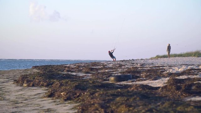 Men stand on the beach during sunset and learn to fly a flying kite, slow motion