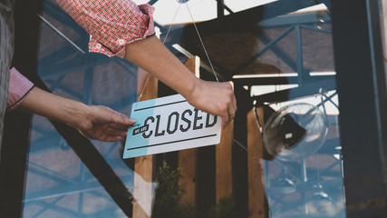 Caucasian female turning sign from open to closed on the entrance door of his small cafe. Out of business - Powered by Adobe