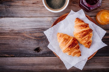 Homemade baked croissants with jam and coffee on wooden rustic background