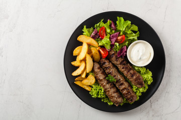 Traditional cevapcici served with baked potatoes. Flat lay. Stone background.