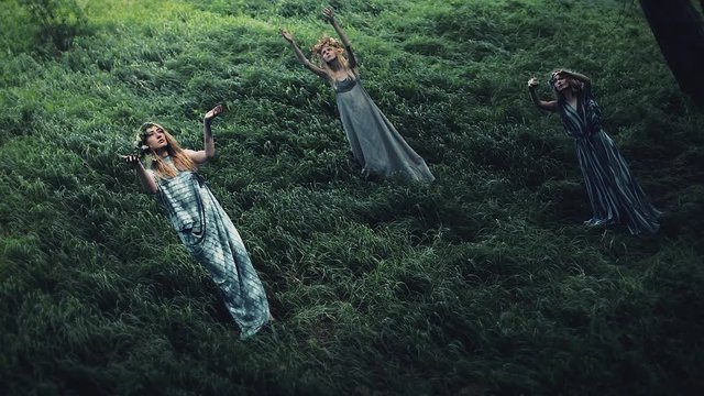 Mystical girls in the woods hold a ritual.They are dressed in long dresses with wreath on the head. Witches, esoteric sessions, magic, divination, otherworldly forces