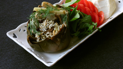 Siyah zemin üzerinde , beyaz tabak içerisinde , pirinç , maydanoz , çamfıstığı ,zeytin yağı harcı doldurulmuş Enginar dolması 