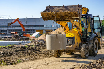 Tractor at the construction site carries a concrete ring for the well