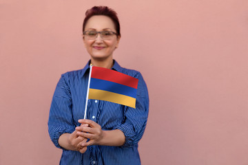 Armenia flag. Woman holding Armenia flag. Nice portrait of middle aged lady 40 50 years old with a national flag over pink wall background outdoors. - 219262135