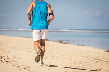 back view of runner training on sand beach near sea, Bali, Indonesia