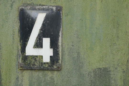  Nummer 4, Ziffer 4, Zahl 4, Hausnummer 4.  Altes schwarzes Blechschild mit weißer Zahl 4 auf grüner, verwitterter Metallwand einer Eisenbahn