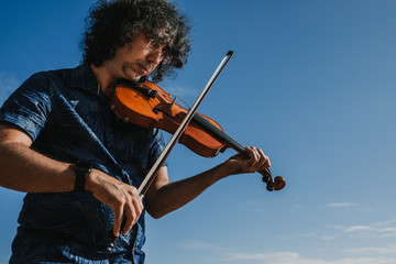 .Young musician playing the violin on a sunny summer day on the beach of Asturias in northern Spain. Expressing emotions and feelings with music. Art. Lifestyle. © lubero
