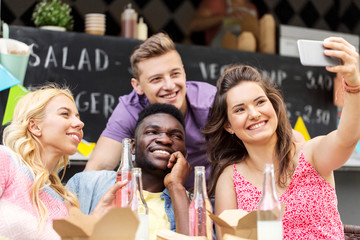 leisure and people concept - happy young friends with food and non alcoholic drinks and taking selfie at food truck