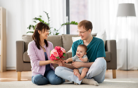 family, parenthood and mothers day concept - happy mother receiving flower bunch from father and baby boy at home