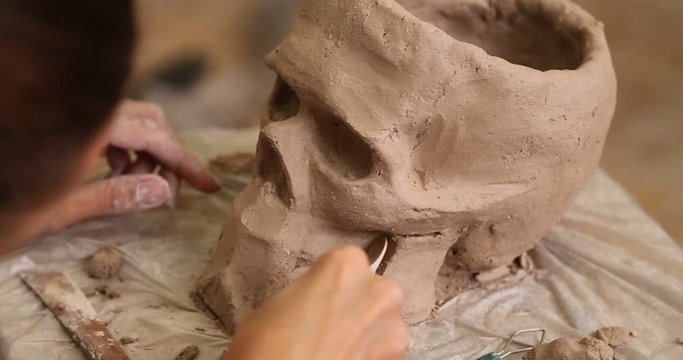 A sculptor modeling a skull out of clay in a sculpting stidio workshop