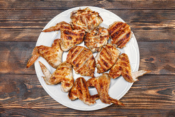 .Grilled chicken wings and hips lie on a white plate on a wooden rustic table.