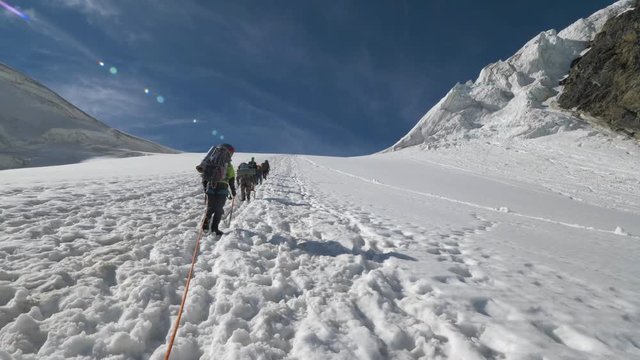 Group of Mountaineers with Backpacks is Roped Together and Ascending on Glacier in Snowy Mountains. Slow Motion