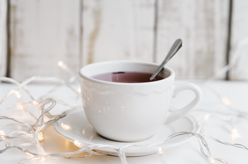 Red hibiscus tea in a small white cup and many yellow lights for home decor on white table