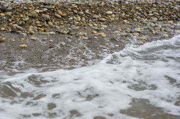 pebble stones on the sea beach, the rolling waves of the sea with foam
