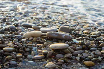 pebble stones on the sea beach, the rolling waves of the sea with foam