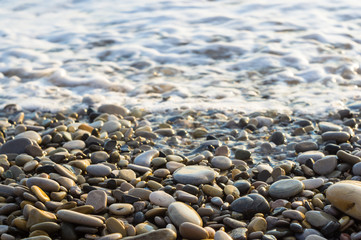 pebble stones on the sea beach, the rolling waves of the sea with foam