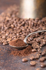 Black roasted coffee grains and ground coffee in spoon lie on a copper table.