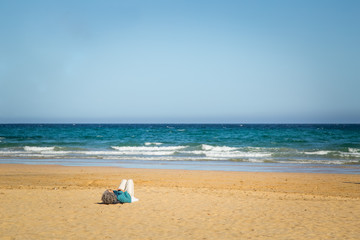 Fototapeta na wymiar Elderly woman lying down on sandy beach with calm water in Fuerteventura.