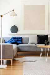 Real photo of bright living room interior with simple poster, metal lamp, grey corner couch and carpet