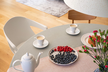 Real photo with high angle of dining table with fresh flowers, jug, coffee cups and plate with fruits