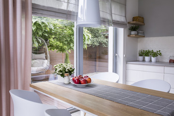 Real photo of a modern dining room interior with a table, plate of apples and view on a terrace...
