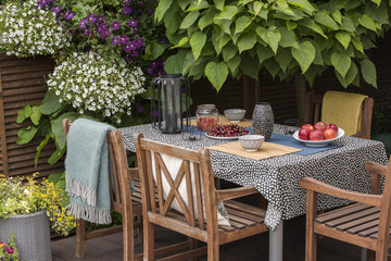 Garden table full of fruit, wooden chairs on a terrace surrounded by plants and flowers