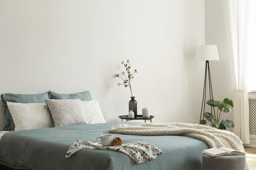 Bedroom interior with sage green and white sheets and cushions and a blanket. Black metal table...