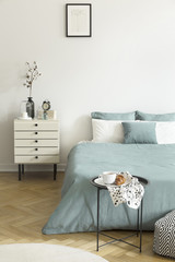 Real photo of a woman's bedroom interior with white walls, parquet floor, pale sage green bedding...