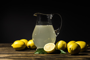 glass jug with organic juice and yellow lemons around on wooden tabletop