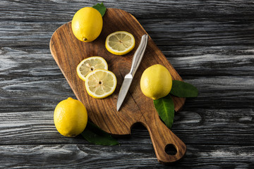 juicy lemons and knife on cutting board on wooden table