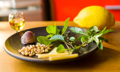 Fresh ingredients for preparing Italian pesto sauce - lemon basil sprigs, peeled seeds of cedar nuts, large garlic clove, Greek olive oil, Parmesan cheese