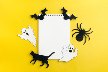 Crafts for Halloween - figures of a spider, bats, ghost and black cat, cut from black and orange paper, scissors, stencils, felt-tip pen, ruler on a yellow background DIY Flat lay Copy space Top view 