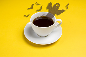 Black coffee in the form of a ghost, witches and bats flying out of a white cup with coffee on a yellow background Flat lay Concept Halloween party Copy space Place for text