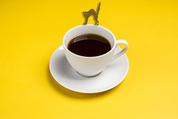 Black coffe in the form of cat walks on a white cup with coffee on a yellow background Flat lay Concept Halloween party Copy space Place for text