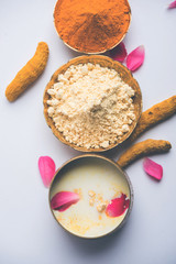 Ayurvedic face pack/mask using Gram Flour/besan, Haldi & milk ubtan placed in brass bowls with rose petals, scrub  and white napkin. selective focus