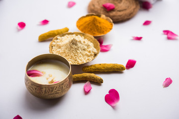 Ayurvedic face pack/mask using Gram Flour/besan, Haldi & milk ubtan placed in brass bowls with rose petals, scrub  and white napkin. selective focus