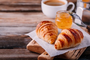 Homemade baked croissants with jam and coffee on wooden rustic background