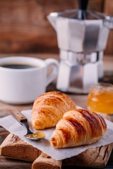 Homemade baked croissants with jam and coffee on wooden rustic background