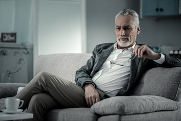 Fototapeta premium Need to think. Pleased retired male person holding glasses in left hand and being deep in thoughts