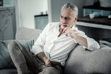 Creating plan. Handsome male person expressing positivity while sitting on the sofa and being deep...