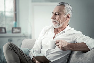 Keep smiling. Cheerful pensioner looking aside while thinking about his plans