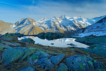 Fototapeta premium Morning in Italian Alps, mountains with smaůe lake in the rock, hills in the clouds, Alp, Gran Paradiso, Italy. Mountain landscpe with blue sky with white clouds.